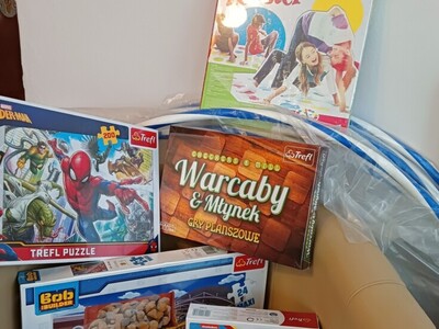 Na fotelu leżą pudełka gier warcawy klasyczne, warcaby obrazkowe, gra Twister, 6 pudełek z różnymi puzzlami.