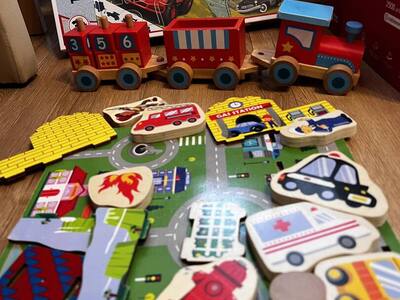 Puzzle drewniane ułożone na podłodze, ciuchcia drewniana z parowozem i dwoma wagonami czerwono pomarańczowa.