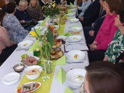 Pracownicy DPS i mieszkańcy siedzący przy zastawionym daniami wielkanocnymi stole.