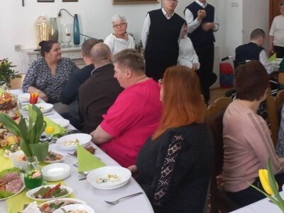 Czworo mieszkańców wykonuje część artystyczną, a pracownicy i pozostali mieszkańcy DPS siedzą za stołem i słuchają występ.