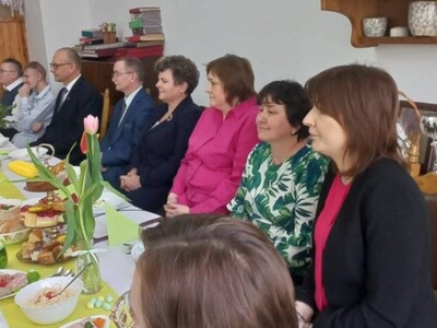 Pracownicy DPS, goście  i mieszkańcy siedzący przy zastawionym daniami wielkanocnymi stole.