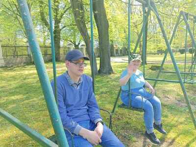 Młody mężczyzna i młoda kobieta w kaszkietach huśtaaja się na huśtawkach wśród zieleni.
