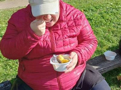 Kobieta siedzi blisko ogniska i zjada pieczonego ziemniaka.