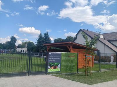 Zdjęcie części padoku z banerem, na którym widnieje podziękowanie za stworzenie padoku. Za płotem i banerem widać drewnianą wiatę.