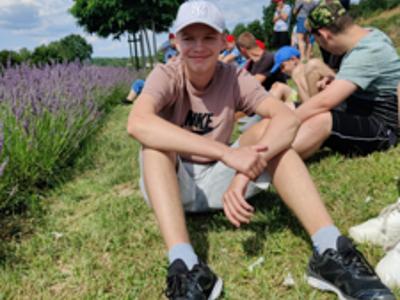 Grupa niepełnosprawnych mieszkańców Domu siedzi na trawie między rzędami kwitnącej lawendy