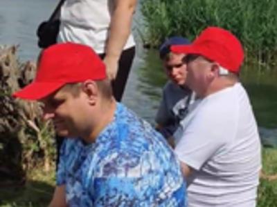 Trzech mężczyzn siedzi na brzegu zalewu kraśnickiego, a w pobliżu stoi opiekunka wycieczki