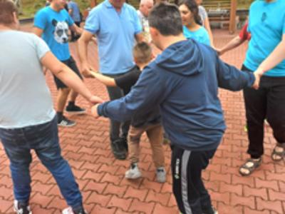 Grupa mieszkańców Domu tańczy w kółeczku do muzyki biesiadnej