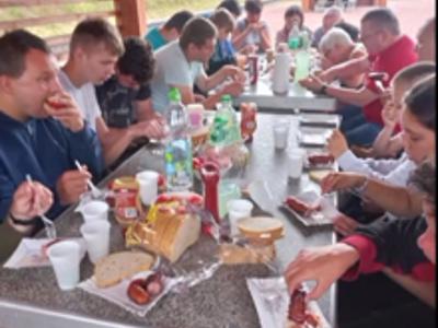 Uczestnicy biwaku siędzą za stołem i konsumują poczęstunek z grilla