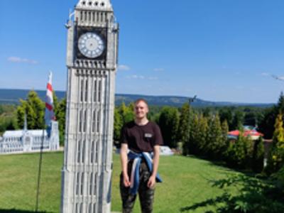 Młody mężczyzna pozuje do zdjęcia na tle miniaturowej wieży z zegarem w Parku Miniatur