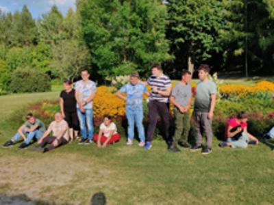 Grupa uczestników wycieczki pozuje do zdjęcia na tle kwiatowego klombu w Muzeum Wsi Kieleckiej