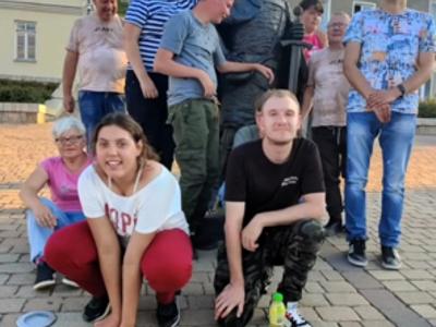 Grupa uczestników wycieczki pozuje do zdjęcia na tle rzeźby króla w Chęcinach.