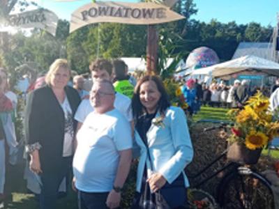 Grupa mężczyzn i kobiet stoi na tle bramy wejściowej dożynkowej.