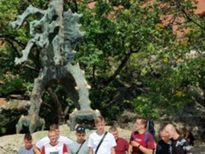 Grupa uczestników wycieczki pozuje do zdjęcia na tle figury smoka wawelskiego.