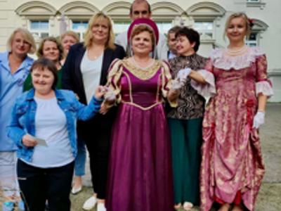 Grupa mieszkańców i pracowników Domu z Dyrektore Elzbietą Spyrą na tle Pałacu