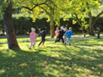 Grupa przedszkolaków podczas gry terenowej w parku.