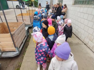 Dzieci w kolorowych kurtkach podczas przejażdżki drewnianą przyczepą przez sad.