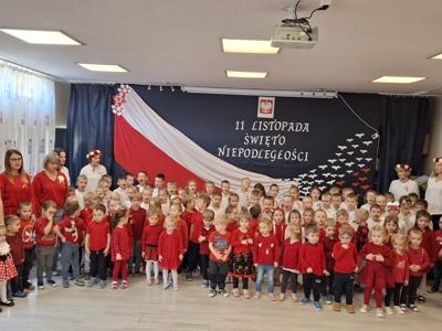 Grupa przedszkolaków wraz z wychowawcami podczas śpiewania hymnu narodowego.