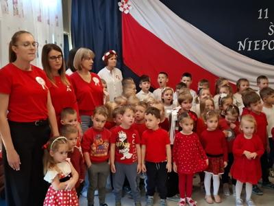 Grupa przedszkolaków wraz z wychowawcami podczas śpiewania hymnu narodowego.