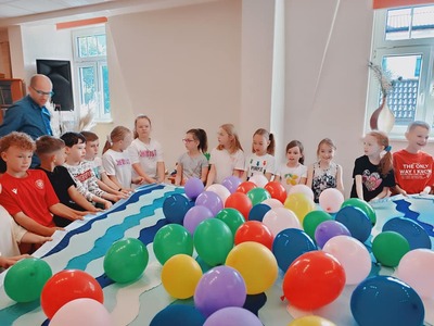 Grupa dzieci wraz z Panem Poetą wykonują zadanie z balonami