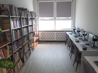Na zdjęciu jest księgozbiór biblioteki oraz komputery.