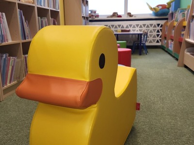 Na zdjęciu jest księgozbiór biblioteki oraz pufy dla dzieci.