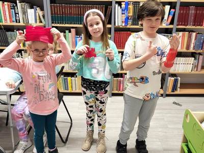 Na zdjęciu znajdują się uczestnicy zajęć. W tle księgozbiór biblioteki.