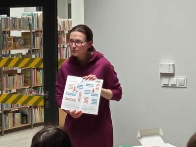 Na zdjęciu znajduje się Pani Pedagog, która pokazuje książki wspierające naukę czytania i pisania.