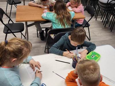 Zdjęcie przedstawia dzieci uczęszczające na warsztaty. Dzieci siedzą przy stole i wykonują prace plastyczne.