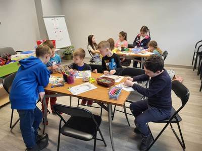 Zdjęcie przedstawia dzieci uczęszczające na warsztaty. Dzieci siedzą przy stole i wykonują prace plastyczne.