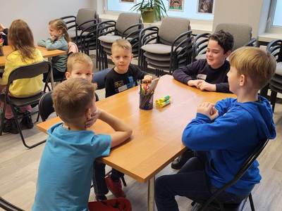 Zdjęcie przedstawia dzieci uczęszczające na warsztaty. Dzieci siedzą przy stole i wykonują prace plastyczne.