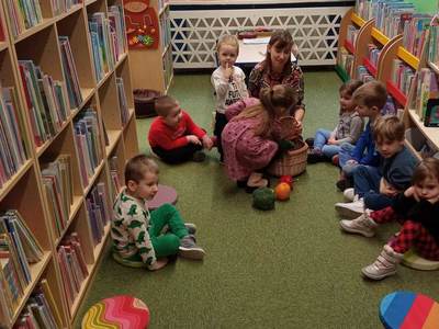 Na zdjęciu znajdują się uczestnicy warsztatów, dzieci siedzą na poduszkach. W tle księgozbiór biblioteki.