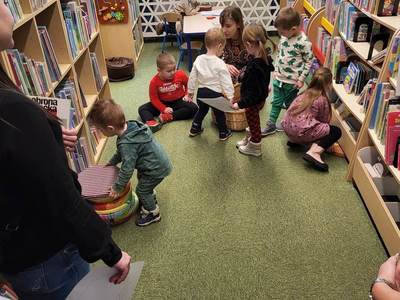 Na zdjęciu znajdują się uczestnicy warsztatów, dzieci siedzą na poduszkach. W tle księgozbiór biblioteki.