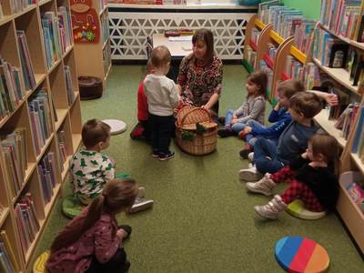Na zdjęciu znajdują się uczestnicy warsztatów, dzieci siedzą na poduszkach. W tle księgozbiór biblioteki.