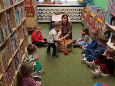 Na zdjęciu znajdują się uczestnicy warsztatów, dzieci siedzą na poduszkach. W tle księgozbiór biblioteki.