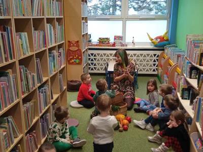 Na zdjęciu znajdują się uczestnicy warsztatów, dzieci siedzą na poduszkach. W tle księgozbiór biblioteki.