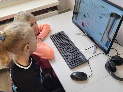 Na zdjęciu znajdują się uczestnicy warsztatów. Dzieci siedzą na krzesłach przy komputerach.
