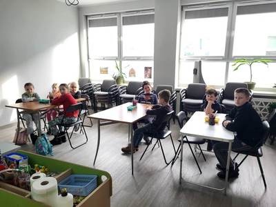 Na zdjęciu znajdują się uczestnicy warsztatów. Dzieci siedzą przy stole i wykonują prace plastyczne.