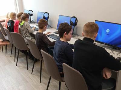 Na zdjęciu znajdują się uczestnicy warsztatów. Dzieci siedzą na krzesłach przy komputerach.