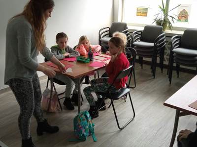 Na zdjęciu znajdują się uczestnicy warsztatów. Dzieci siedzą przy stole i wykonują prace plastyczne.
