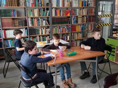 Na zdjęciu znajdują się uczestnicy warsztatów. Dzieci siedzą przy stole i wykonują prace plastyczne.