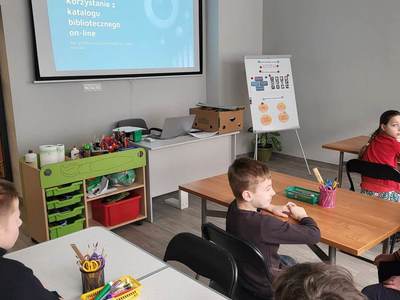 Na zdjęciu znajdują się uczestnicy warsztatów. Dzieci siedzą przy stole i wykonują prace plastyczne.