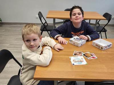 Na zdjęciu znajdują się uczestnicy bibliotecznych spotkań. Uczestnicy siedzą przy stole i grają w gry planszowe.