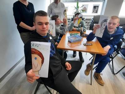 Na zdjęciu znajdują się uczestnicy warsztatów. Młodzież siedzi przy stole i wykonuje prace plastyczne.