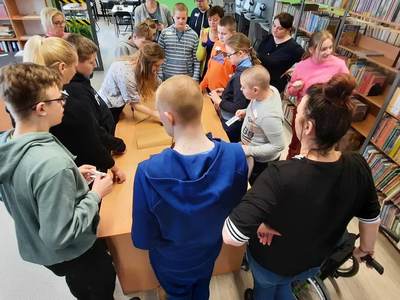 Na zdjęciu znajdują się uczestnicy warsztatów. Młodzież  stoi dookoła stołu i patrzą na plakat sieć przyjaźni.