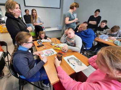 Na zdjęciu znajdują się uczestnicy warsztatów. Młodzież siedzi przy stole i wykonuje prace plastyczne.