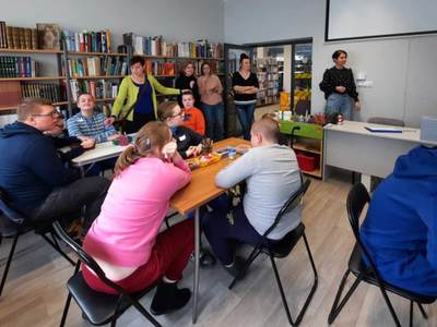 Na zdjęciu znajdują się uczestnicy warsztatów. Młodzież siedzi przy stole i wykonuje prace plastyczne.