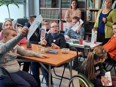 Na zdjęciu znajdują się uczestnicy warsztatów. Młodzież siedzi przy stole i wykonuje prace plastyczne.