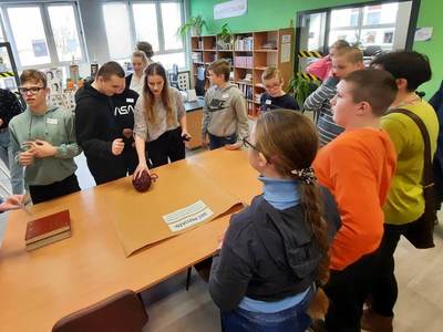 Na zdjęciu znajdują się uczestnicy warsztatów. Młodzież siedzi na poduszkach pomiędzy regałami.