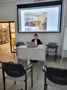 Na zdjęciu znajduje się jedna osoba. W tle prezentacja multimedialna.