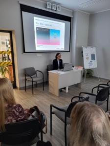 Na zdjęciu znajduje się jedna osoba. W tle prezentacja multimedialna.